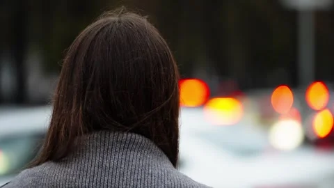 Rear view of a lone figure in a gray knit sweater facing a street at dusk, with Stock Footage 327732368