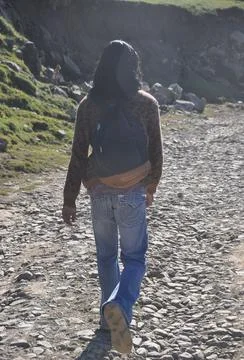 Rear view of a long haired young man walking on rough road with backpack  Stock Photos
