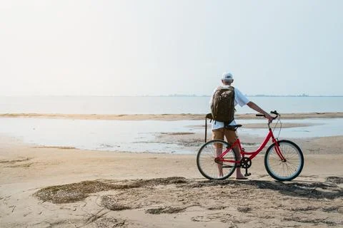 Rear view of man with backpack standing and holding bike on seafront Stock Photos