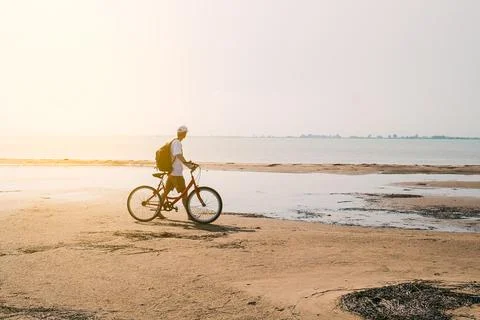 Rear view of man with backpack standing and holding bike on seafront Stock Photos
