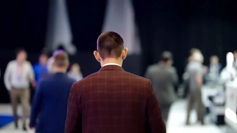 Rear view of a man in a checkered suit amid a blurred crowd at a professional Stock Footage 325670978