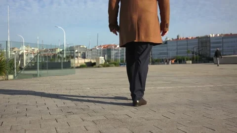 The rear view of a man in a classic coat and trousers walks down the road in the Stock Footage 221804377