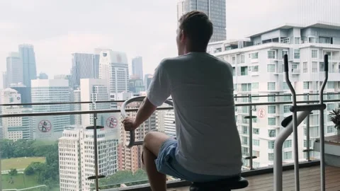 Rear view of man exercising on spinning bicycle on modern outdoor balcony Stock-Footage 280943176