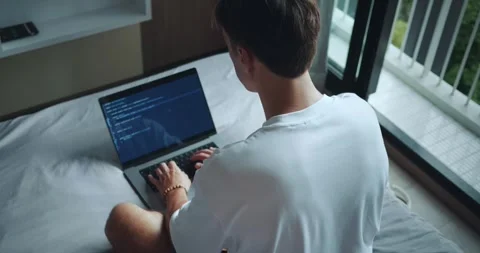 Rear view man freelancer programmer sitting on bed in bedroom and working on Stock Footage 251788236