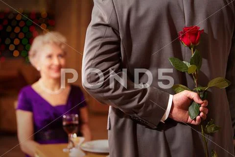 Rear view of man holding red rose in hand on background of intrigued female Stock Photos
