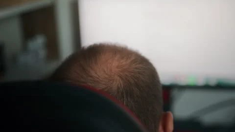 Rear view of a man intently looking at a large computer monitor in a home o.. Video stock 327573907