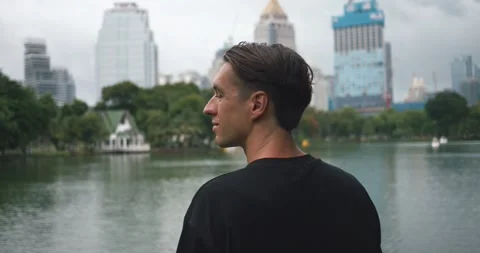 Rear view man looking at lake in public city park with modern skyscrapers Stock Footage 251788075