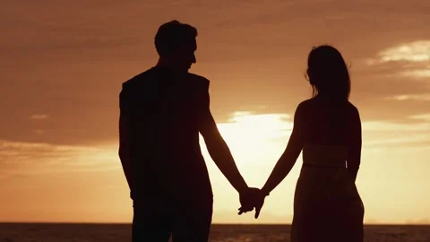 Rear view of man in love takes a woman's hand on a date against an orange sunset Stock Footage 251021953
