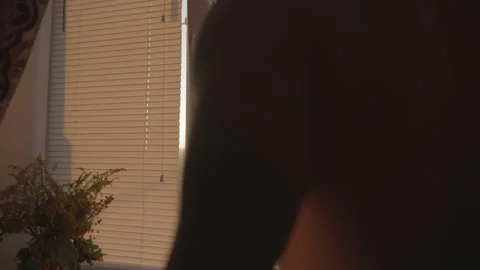 Rear view of a man opening window blinds in dark cinematic room Видео 343629700