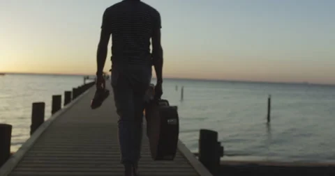 Rear view of man picking up his gig bag and walking on pier during sunset Stock Footage