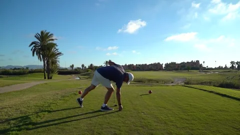 Rear view of a man placing a golf ball on the ground and performing a swing.. Stock Footage 252603914