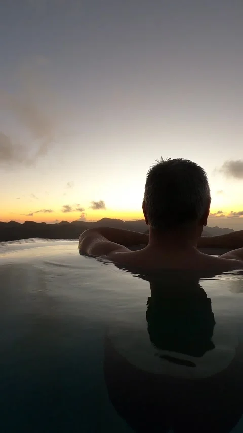 Rear view of a man relaxing in an infinity pool at sunset, gazing at landscape Video stock 313143552