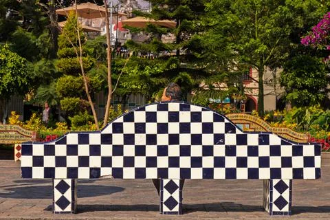 Rear view of man sitting alone on checkered tiled bench in main square Stock Photos