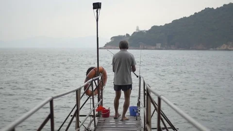 Rear view of man standing at the edge of the jetty while fishing in the sea Stock Footage 69740451