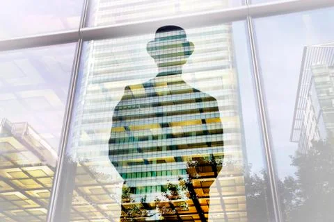 Rear view of man standing at window, reflection of illuminated skyscraper. Fotos de archivo
