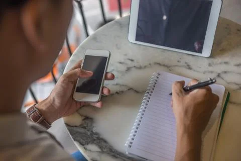 Rear view of man using phone and writing notes Foto stock