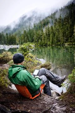 Rear view of man using tablet computer while sitting at lakeshore Stock Photos