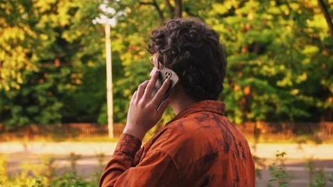 Rear view of man walking down street of central district of city and talking on Stock Footage 243375733