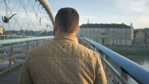 Rear view of man walking through the footbridge over the river, steadicam shot Vídeo Stock 72775682
