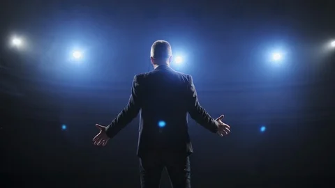 Rear view of men speaking through a microphone in dark conference hall. Person Видео 121592361