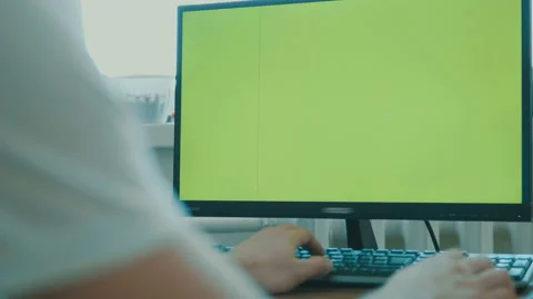 Rear view of a middle-aged man sitting in front of a large screen monitor. Green Stock Footage 86324419