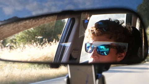 Rear view mirror closeup of face of young man driving at sunset Stock Footage 112121516
