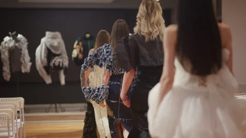 Rear view of models wearing different dresses walking down a runway with empty Stock Footage 335351200