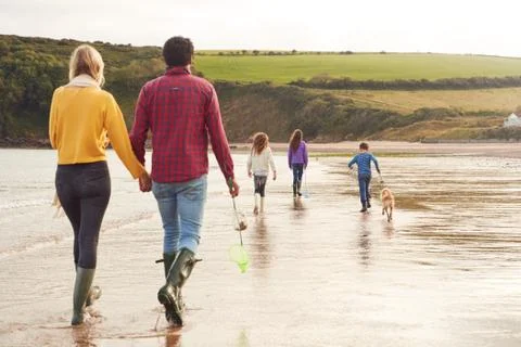 Rear View Of Multi-Cultural Family With Pet Dog Walking Along Beach Shoreline On Stock Photos