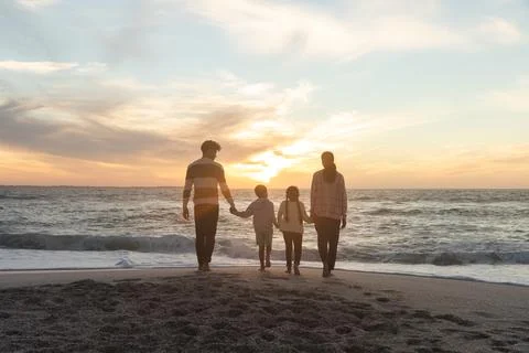 Rear view of multiracial family walking together towards shore at beach during Stock Photos