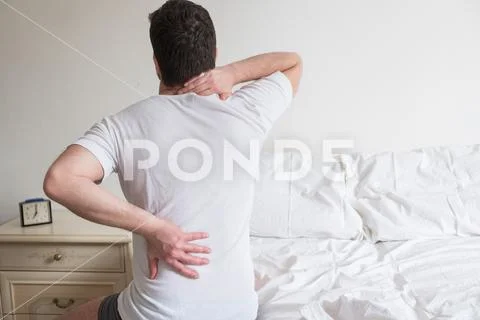 Rear view of one man sitting on bed having back pain Stock Photos