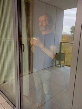 Rear view from outside to inside of man with cup standing by window, looking out Stock Photos