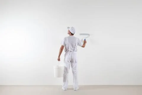 Rear view of painter man looking at blank wall, with paint roller and bucke.. Foto stock