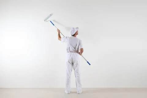 Rear view of painter man looking at blank wall, with paint roller stick, is.. Stock Photos