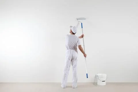 Rear view of painter man looking at blank wall, with paint stick roller and.. Stock-Fotos