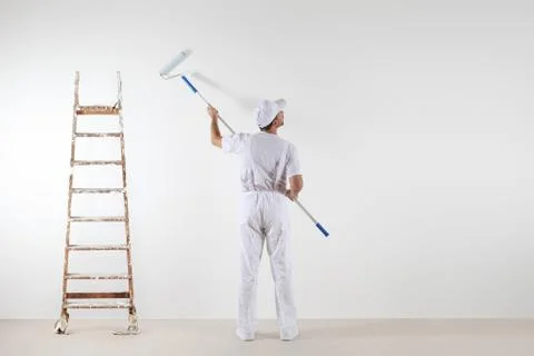 Rear view of painter man looking at blank wall, with paint stick roller and.. Stock-Fotos