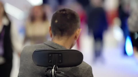 Rear view of a person using a motorized wheelchair navigating a bright, crowded Video stock 325670722