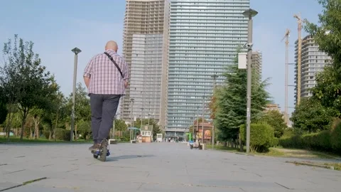 Rear view of plus size man riding e-scooter in the city. Male driving electric Stock Footage 255052149