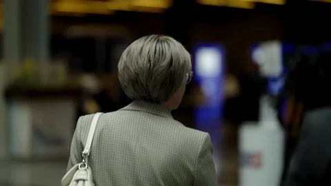 Rear view of professionals walking through a modern lobby, a woman carrying a Video stock 325669885