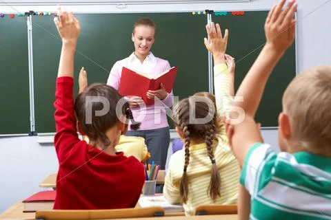 Rear view of pupils raising arms during the lesson with teacher looking at them Stock Photos