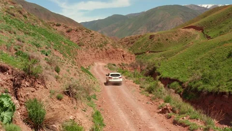 A rear view of a receding white SUV driving along a dusty, dry mountain road Stock-Footage 276645694