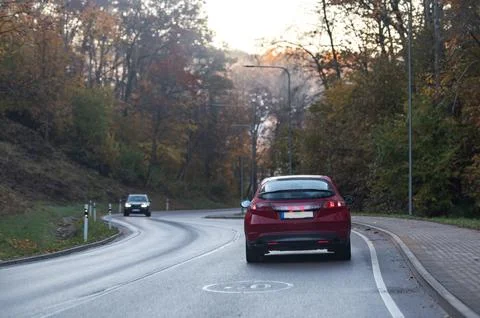 Rear view of a red car on a bend in an autumn road, speed limit sign Stock Photos