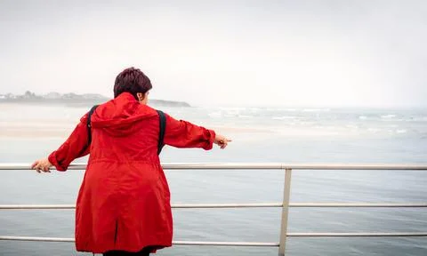 Rear view of a reflective woman red trench coat contemplating the sea on a be Stock Photos