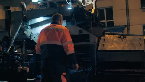 Rear view of a road worker in front of a passing asphalt paver. Repair of a city Stock Footage 153380290