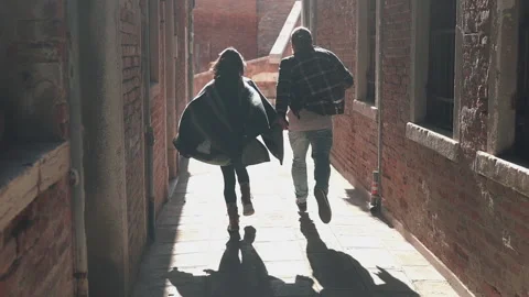 Rear view of romantic mixed race couple running at sunrise in Venice. Happy Stock Footage 130973526