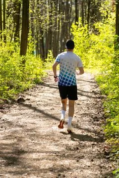Rear view of a runner jogging along a sunlit forest trail Stock Photos
