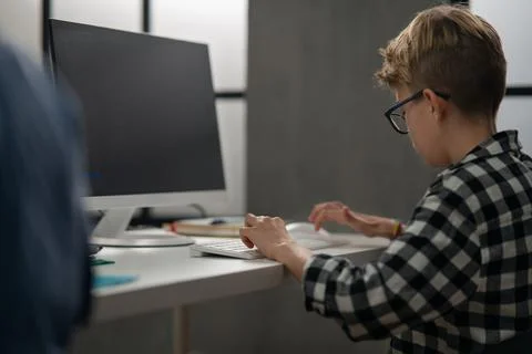Rear view of schoolboy using computer in classroom at school 스톡 사진