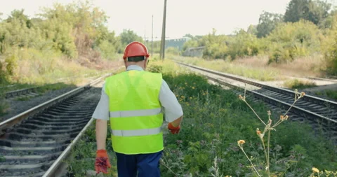 Rear view of senior engineer in uniform walks at tracks out of town in summer Stock Footage 135573472