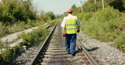 Rear view of senior engineer in uniform walks along track out of town in summer Video stock 135573775