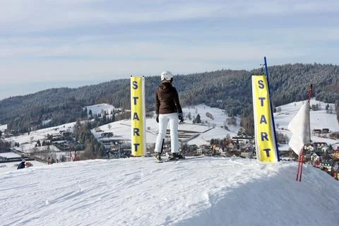 Rear view of a skier standing between yellow start flags atop a snowy slope. Stock Photos