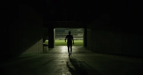 Rear view of soccer player walking to outdoor football stadium, dark corridor Stock Footage